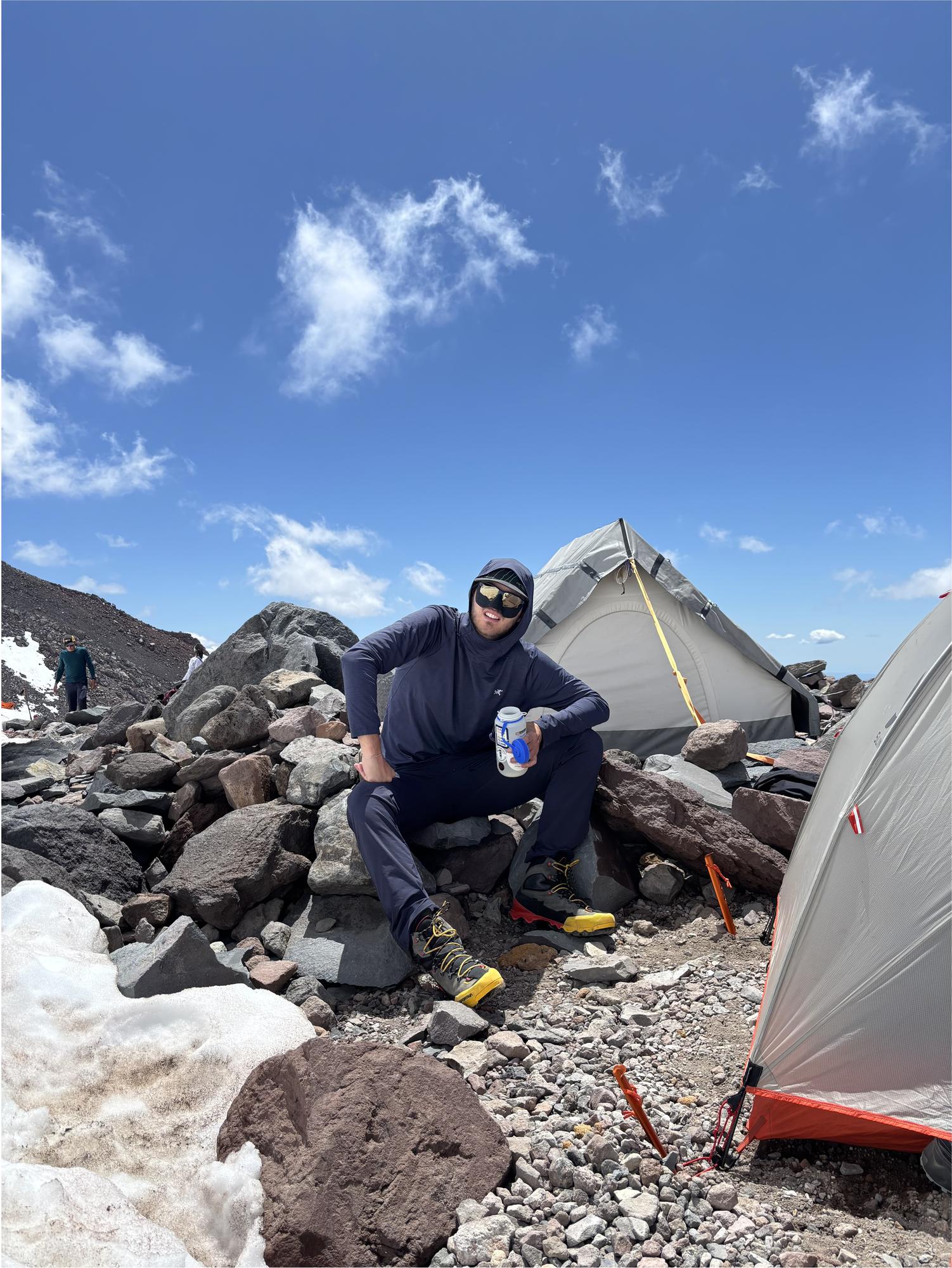 A high alpine camp with tents pitched among volcanic rock and patches of snow