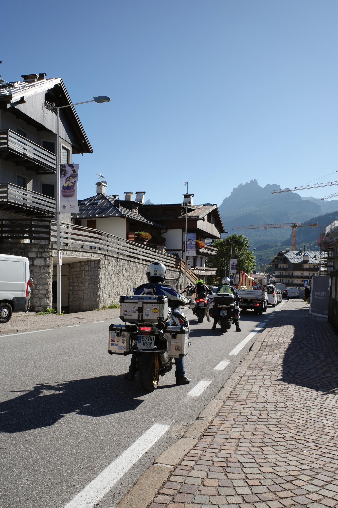 Loaded adventure motorcycles riding through a Dolomites town toward a mountain pass