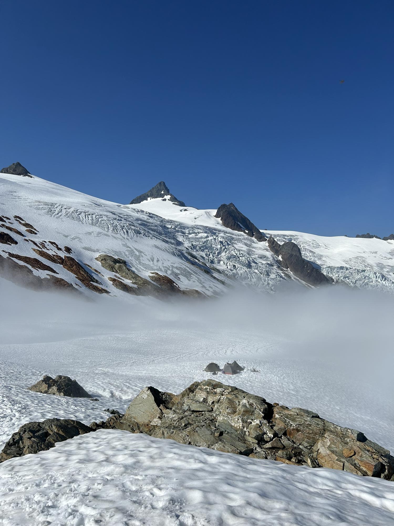 A glaciated alpine basin with mist drifting across snowfields below rocky spires