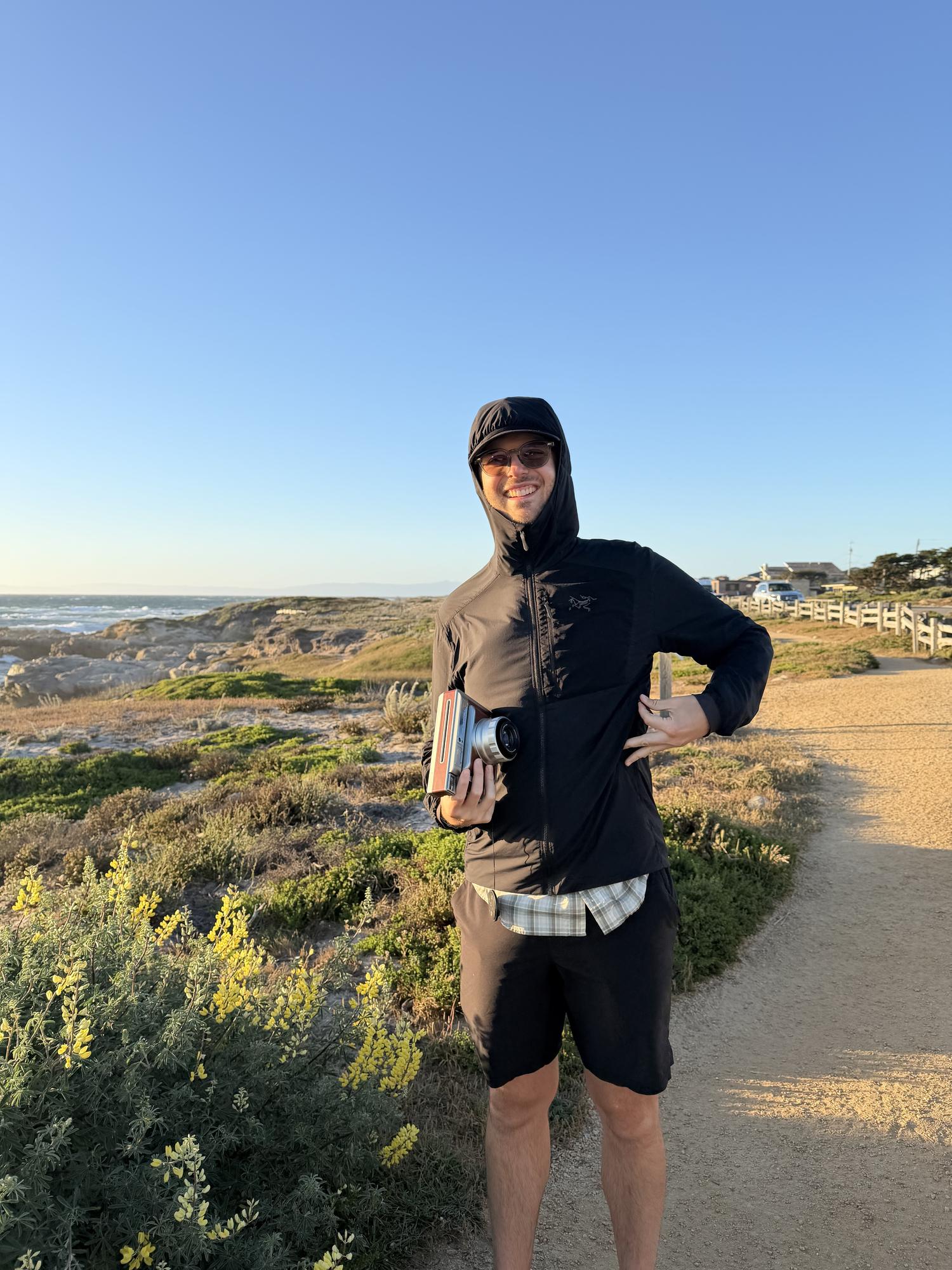 Trail runner in a black shell on a coastal path at golden hour above the Pacific