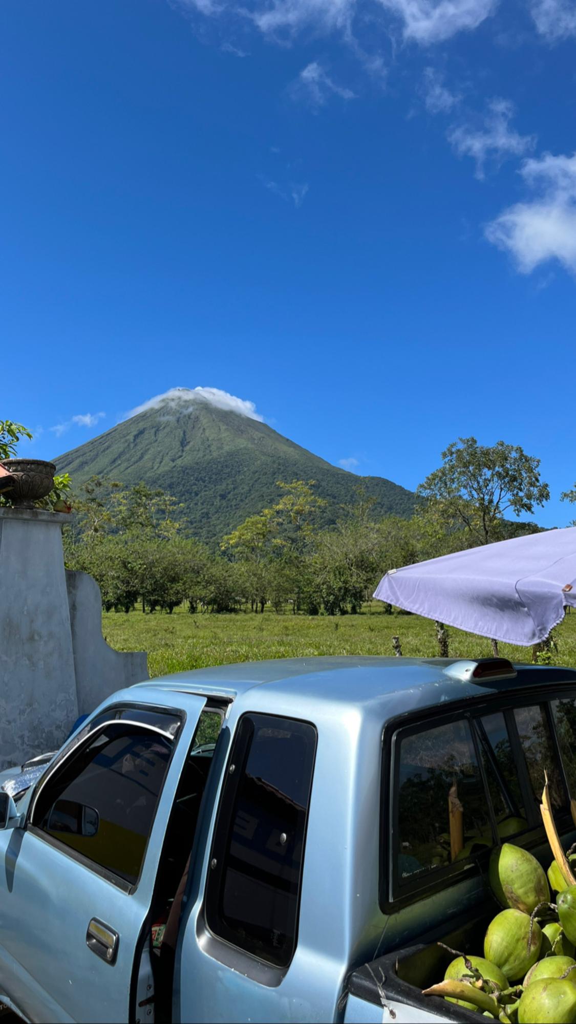A steep conical volcano wreathed in cloud rising above green tropical farmland