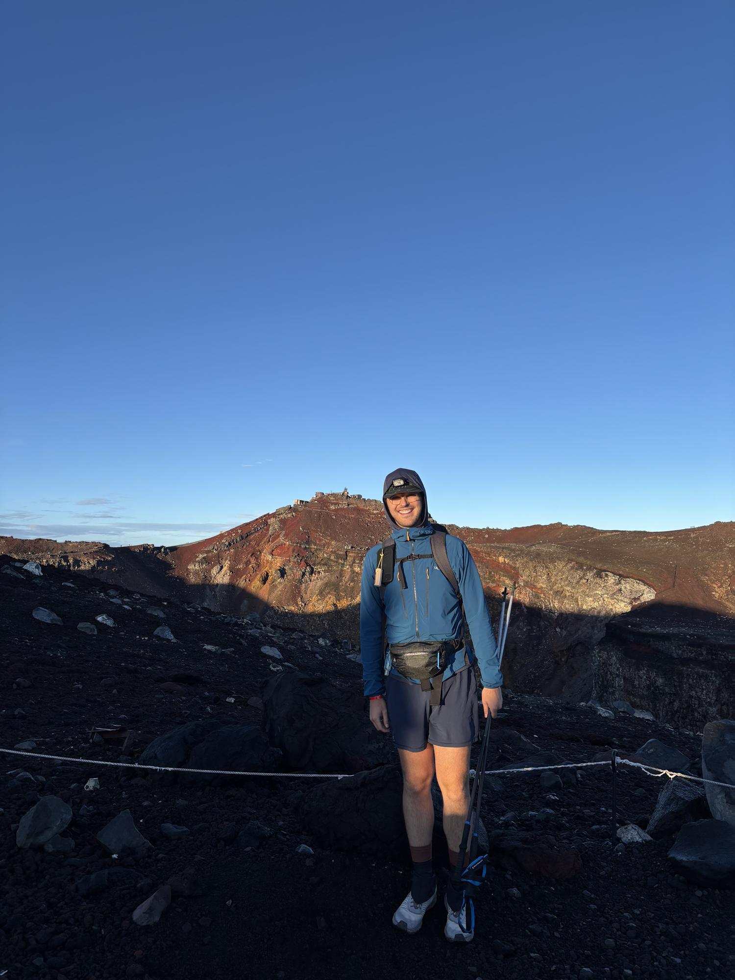 Jake Heller with a pack on a volcanic crater rim at sunrise, red cinder slopes behind